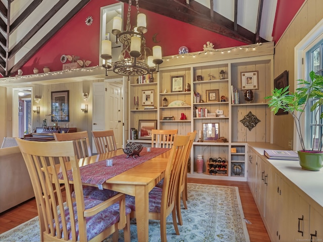 dining space with a notable chandelier, light hardwood / wood-style flooring, lofted ceiling with beams, and wooden walls