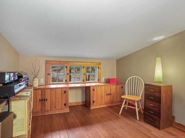 office area featuring built in desk, vaulted ceiling, and light hardwood / wood-style floors