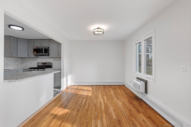 kitchen featuring gray cabinets, a wall unit AC, decorative backsplash, light hardwood / wood-style flooring, and appliances with stainless steel finishes