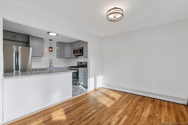 kitchen with stainless steel appliances, gray cabinetry, light wood-type flooring, hanging light fixtures, and light stone counters