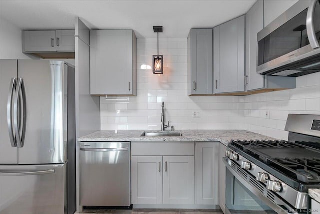 kitchen with appliances with stainless steel finishes, gray cabinetry, hanging light fixtures, light stone countertops, and sink