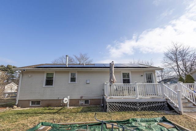 back of property featuring a deck, solar panels, and a yard