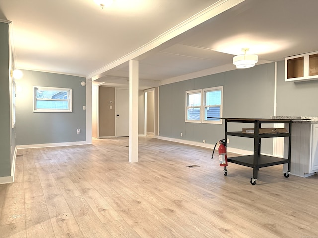 basement featuring a wealth of natural light, crown molding, and light hardwood / wood-style floors