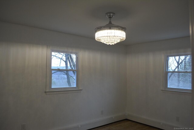 spare room featuring a healthy amount of sunlight, dark hardwood / wood-style floors, and a chandelier