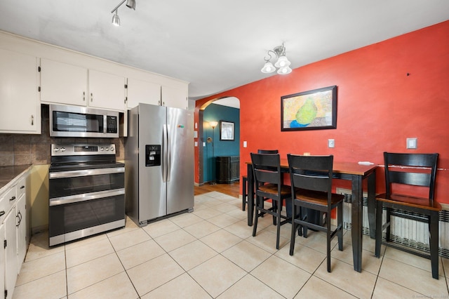 kitchen with appliances with stainless steel finishes, tasteful backsplash, white cabinetry, light tile patterned floors, and track lighting