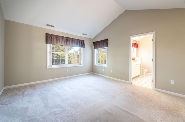 unfurnished bedroom with vaulted ceiling, connected bathroom, and light colored carpet