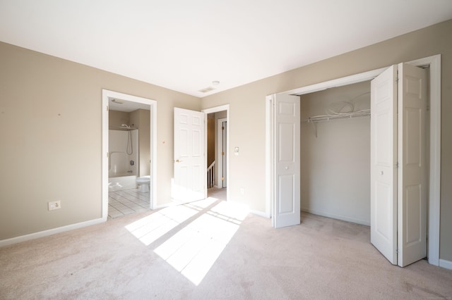 unfurnished bedroom with a closet, ensuite bathroom, and light carpet