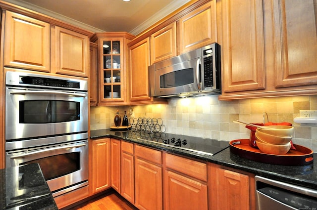 kitchen featuring appliances with stainless steel finishes, crown molding, backsplash, and dark stone counters