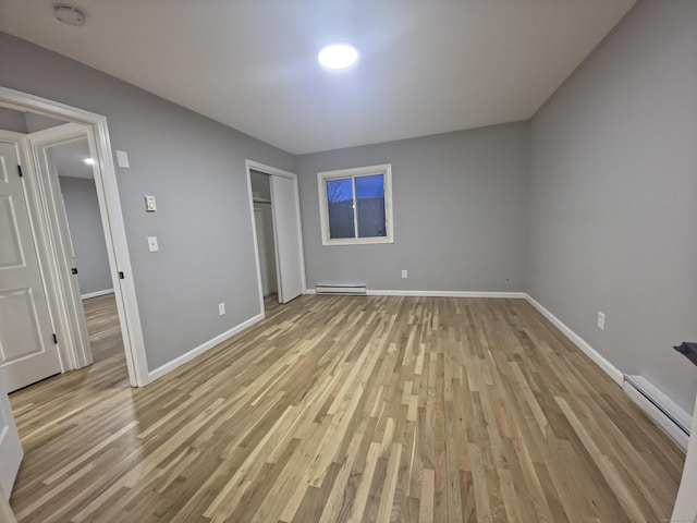 unfurnished bedroom with a baseboard radiator, a closet, a baseboard heating unit, light wood-style floors, and baseboards