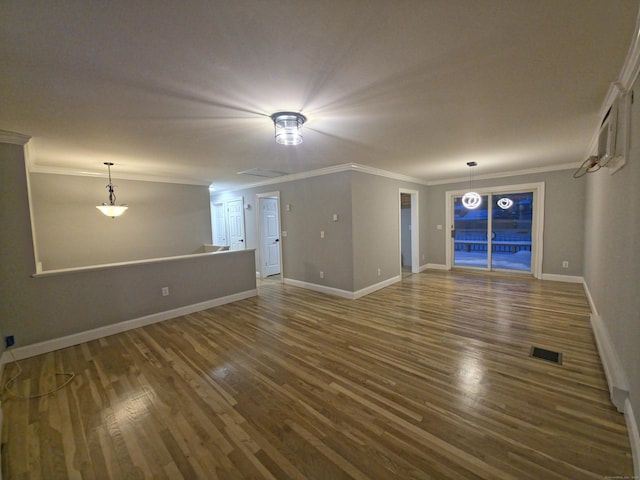 unfurnished living room featuring baseboards, wood finished floors, visible vents, and crown molding