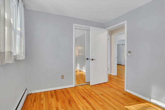 unfurnished bedroom with baseboard heating, light hardwood / wood-style floors, and a closet