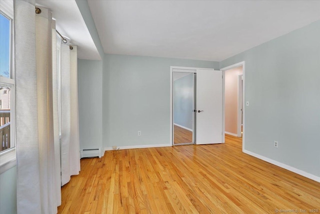 unfurnished bedroom with baseboard heating, light hardwood / wood-style floors, and a closet