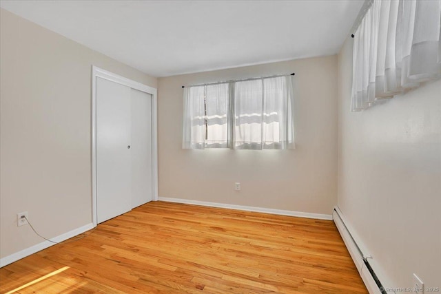 unfurnished bedroom with a baseboard heating unit, light wood-type flooring, and a closet