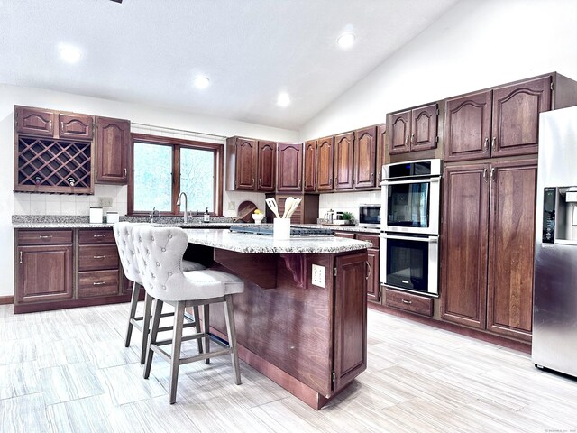 kitchen with a breakfast bar area, appliances with stainless steel finishes, backsplash, lofted ceiling, and a center island