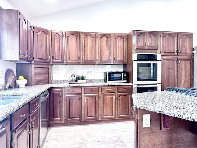 kitchen featuring vaulted ceiling, stainless steel appliances, light stone counters, and tasteful backsplash