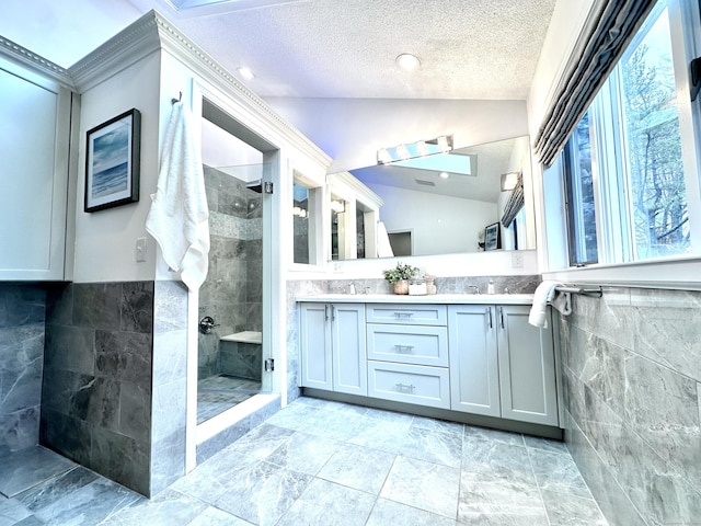 bathroom featuring a textured ceiling, lofted ceiling, vanity, tile walls, and a tile shower