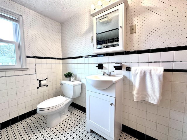 bathroom with toilet, tile patterned flooring, tile walls, a textured ceiling, and vanity