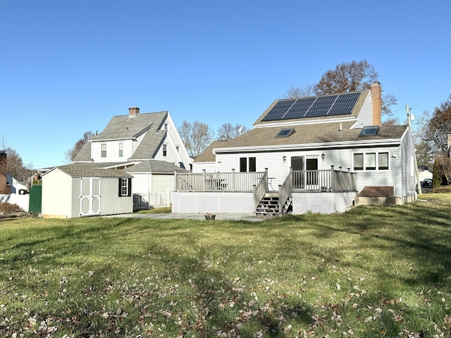 back of property with a lawn, a storage unit, solar panels, and a wooden deck