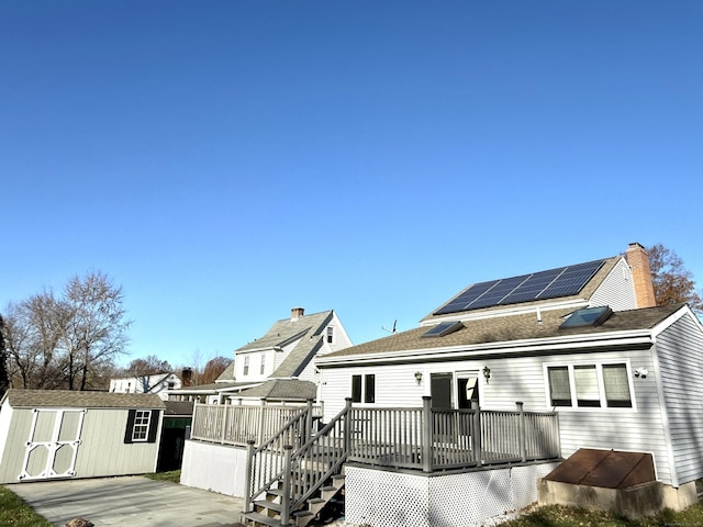 back of house featuring a deck, a storage unit, and solar panels