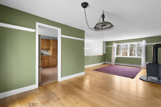 unfurnished living room featuring a wood stove, a baseboard heating unit, a notable chandelier, and light wood-type flooring