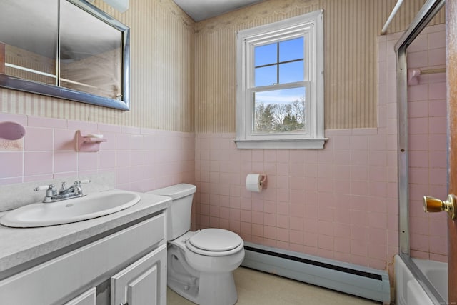 full bathroom featuring bath / shower combo with glass door, tile walls, vanity, baseboard heating, and toilet