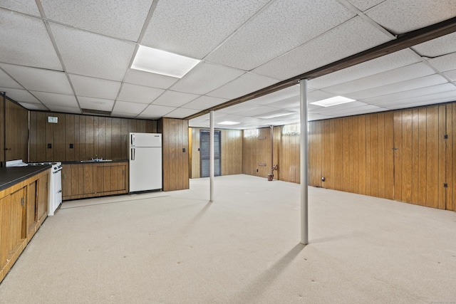 basement with a paneled ceiling, wooden walls, light colored carpet, and white fridge