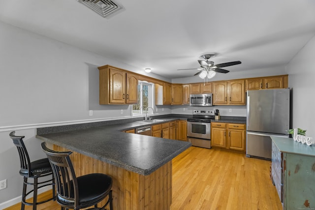 kitchen with kitchen peninsula, sink, light hardwood / wood-style flooring, a breakfast bar area, and stainless steel appliances