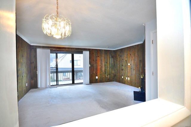 spare room featuring wood walls, a water view, an inviting chandelier, ornamental molding, and carpet flooring