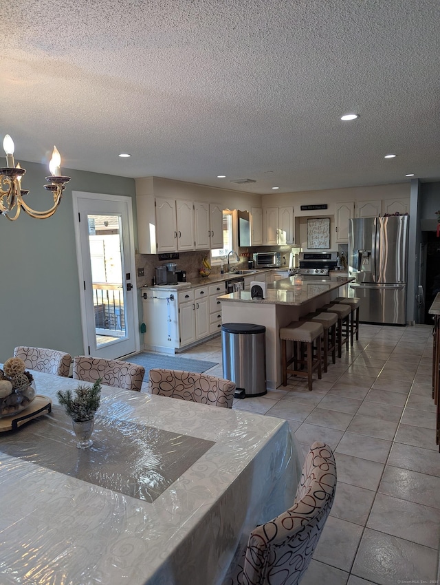 kitchen featuring a textured ceiling, appliances with stainless steel finishes, a center island, backsplash, and a breakfast bar