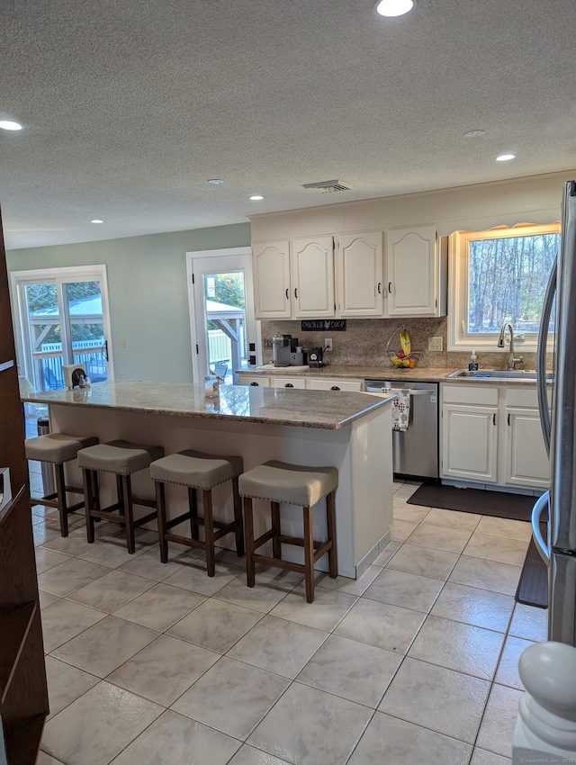 kitchen featuring white cabinetry, appliances with stainless steel finishes, a kitchen breakfast bar, a kitchen island, and sink