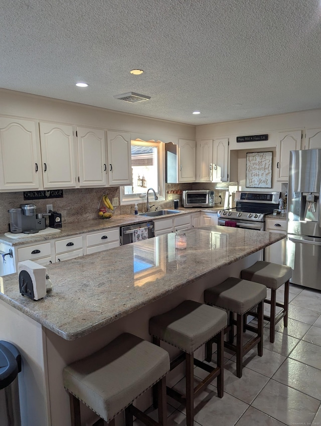 kitchen with light stone countertops, white cabinetry, appliances with stainless steel finishes, and a center island