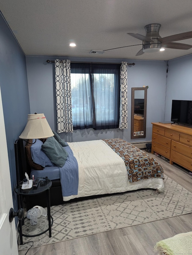 bedroom with a textured ceiling, ceiling fan, and hardwood / wood-style floors