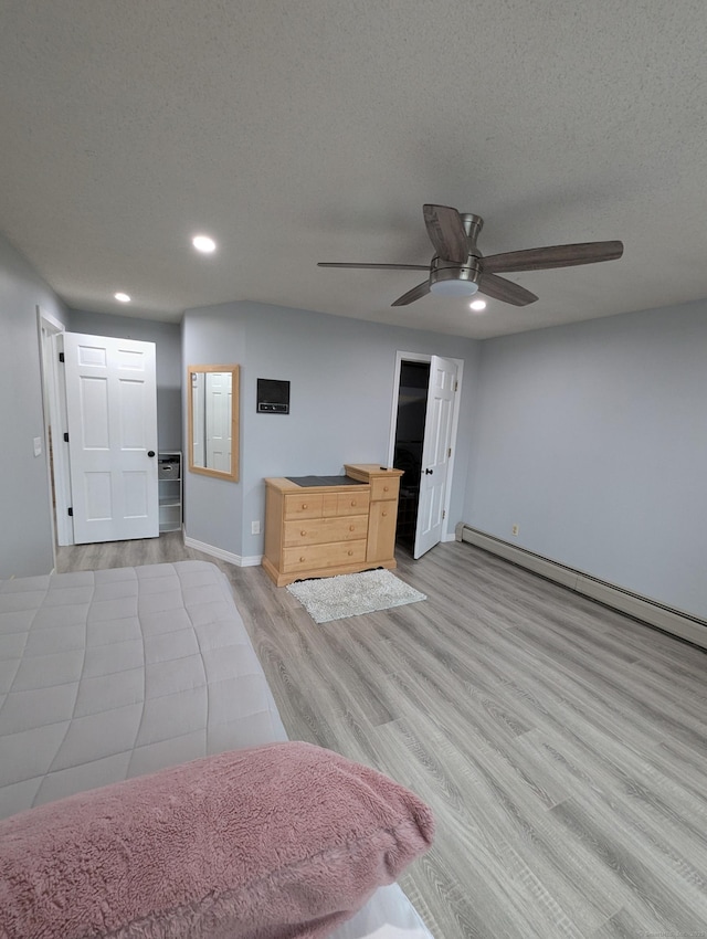 unfurnished bedroom with ceiling fan, a textured ceiling, a baseboard heating unit, and light hardwood / wood-style flooring