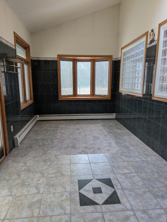 tiled empty room featuring lofted ceiling, baseboard heating, and tile walls