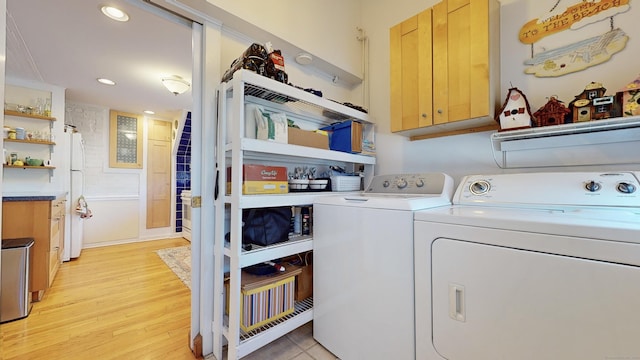 laundry room with light hardwood / wood-style floors, cabinets, and washing machine and clothes dryer