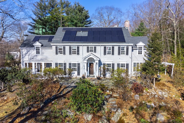 view of front facade with roof mounted solar panels, roof with shingles, and a chimney