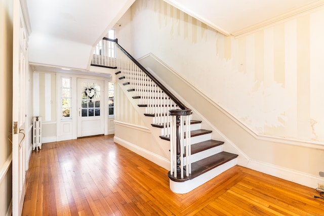 staircase with crown molding, radiator heating unit, wood-type flooring, and baseboards