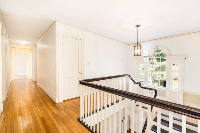 hallway with light wood-style flooring, a notable chandelier, and an upstairs landing