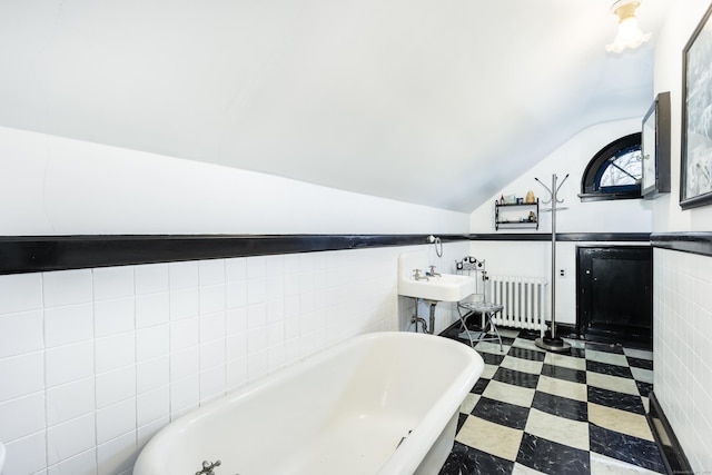 bathroom featuring tile walls, lofted ceiling, radiator, a freestanding tub, and tile patterned floors