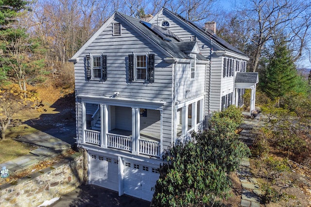 view of side of home featuring driveway, a chimney, and an attached garage