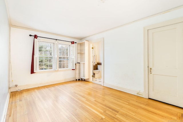 spare room featuring light wood-type flooring, crown molding, and baseboards