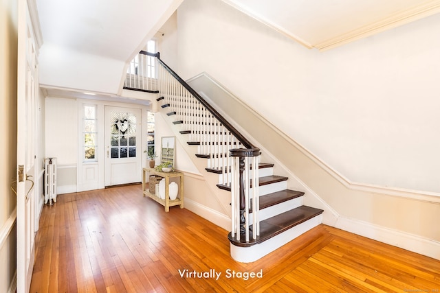 stairway with a towering ceiling, baseboards, radiator heating unit, wood-type flooring, and crown molding