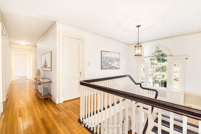 hall featuring light wood-style flooring, a notable chandelier, and an upstairs landing