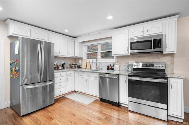 kitchen with appliances with stainless steel finishes, light hardwood / wood-style flooring, white cabinets, and sink