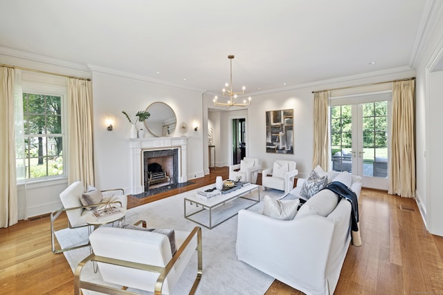 living room featuring french doors, a fireplace, ornamental molding, a chandelier, and light hardwood / wood-style flooring