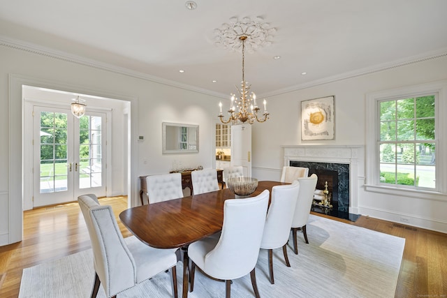 dining space featuring french doors, a fireplace, light hardwood / wood-style floors, a notable chandelier, and crown molding