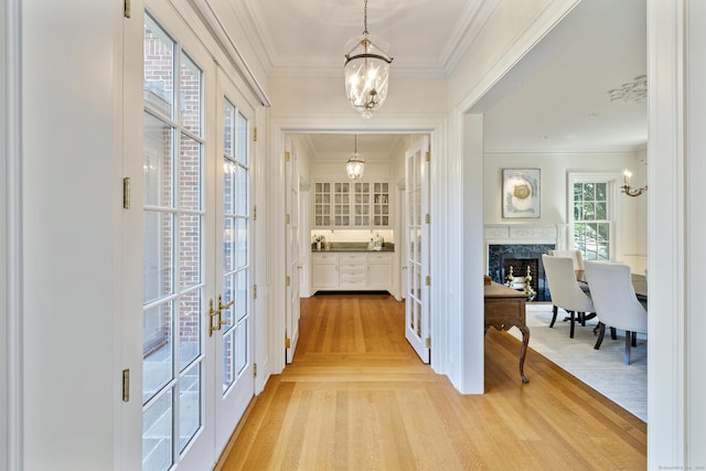 hallway featuring french doors, a notable chandelier, crown molding, and light hardwood / wood-style floors