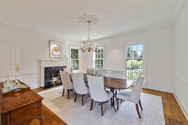 dining space with light hardwood / wood-style floors, a chandelier, ornamental molding, and a premium fireplace