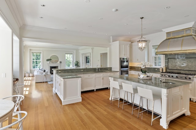 kitchen featuring pendant lighting, white cabinetry, tasteful backsplash, light hardwood / wood-style floors, and a center island with sink