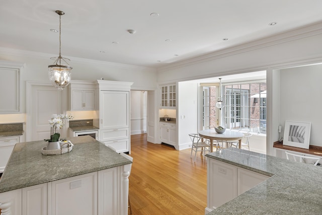 kitchen featuring a kitchen island, an inviting chandelier, light hardwood / wood-style flooring, white cabinets, and stone countertops